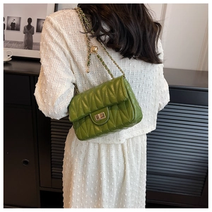 Close-up of green quilted leather bag with gold chain and ball detail worn by a model