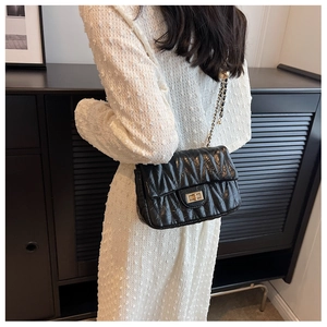 Detail of black matelassé leather shoulder bag with gold chain strap and twist lock