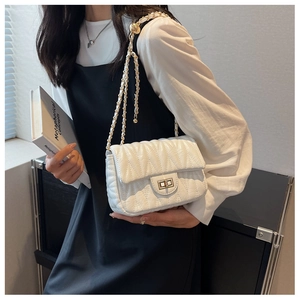 Detail of a beige quilted leather crossbody bag with a gold twist lock and chain strap