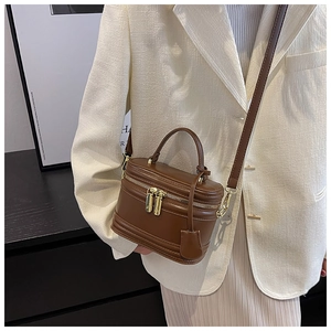 Brown leather cylinder crossbody bag featuring a round top handle and gold hardware detail