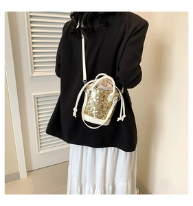 Detail of a mini bucket bag with gold sequins, drawstring closure, and white leather trim