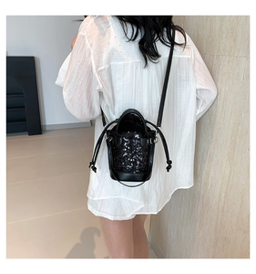 Detail of black sequined bucket bag with drawstring closure and chain strap on model