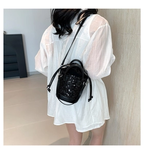 Detail of a black sequined drawstring bucket bag worn crossbody over a white shirt
