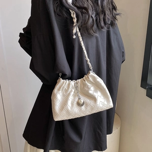 Chic off-white woven cloud bag with pearl charms and chain strap carried by a model