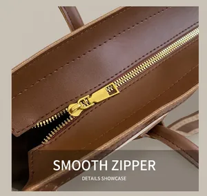 Detailed close-up of smooth golden metal zipper and stitching on brown leather tote bag