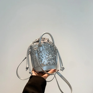 Silver sequin bucket bag with drawstring liner and crossbody strap shown handheld