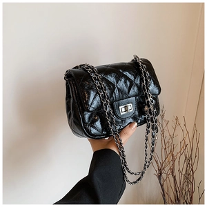 Close-up of black quilted glossy handbag with silver metal turn-lock and chain strap
