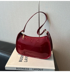 Detailed view of glossy burgundy patent leather hobo bag with gold zipper and hardware
