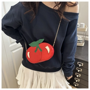 Close-up of red cherry-shaped shoulder bag with green leaves and gold chain strap
