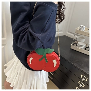 Detail of creative cherry shaped crossbody bag with green leaves and gold metal chain