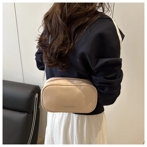 Détail du sac polochon beige avec bandoulière chaîne argentée et logo texte tendance