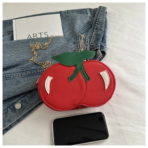 Detailed view of the red cherry-shaped mini bag with gold chain on denim fabric