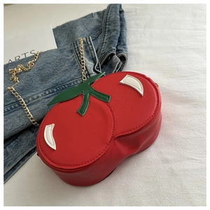Detail of red cherry shaped shoulder bag with leaf accents and gold metal chain strap