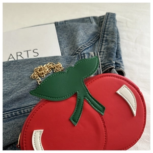 Detail of red cherry handbag with green leather leaves and golden chain strap