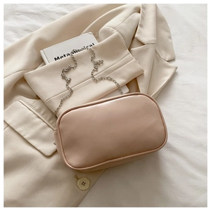 Detail of minimalist cream PU leather crossbody bag with slim silver chain on beige blazer