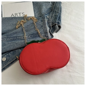 Detailed view of creative cherry shaped red handbag with green leaf and gold chain strap