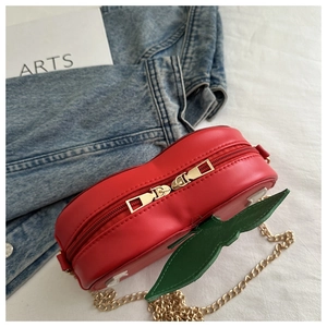 Detail of red cherry-shaped handbag with green leaf decor and gold metal chain strap