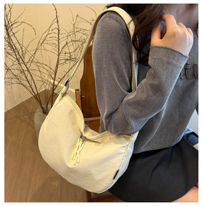 Close-up of cream nylon crescent bag with zipper tassel detail on a shoulder strap