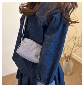 Detail of light purple pleated crossbody bag with FANYISSA label and metal logo charm