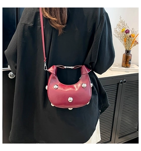 Close-up of matte burgundy crescent bag featuring decorative silver metal rivets and strap