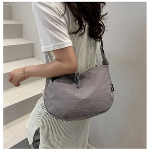 Detail of grey nylon crossbody bag featuring drawstring texture and branded fabric label