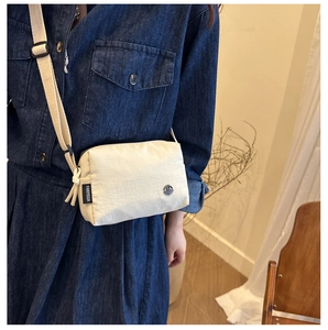 Détail du sac bandoulière en nylon blanc cassé avec étiquette tissée et logo métallique