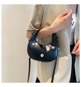 Close-up of black leather crescent bag with large silver stud accents on model