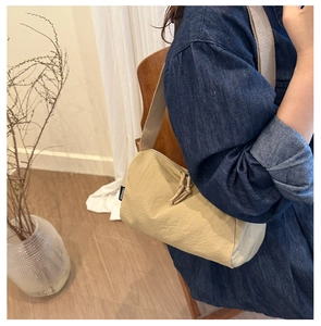 Détail d'un sac bandoulière en nylon beige avec étiquette et tirette de zip nouée