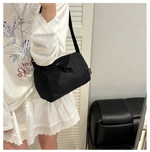 Detailed shot of black nylon crossbody bag with fabric strap and brand label on model