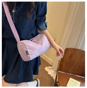 Model wearing a light purple nylon cylinder crossbody bag with adjustable strap detail