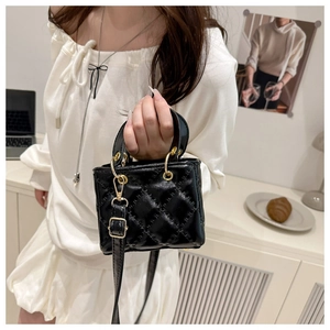 Detail view of mini black quilted handbag with elegant gold ring handle and chain strap
