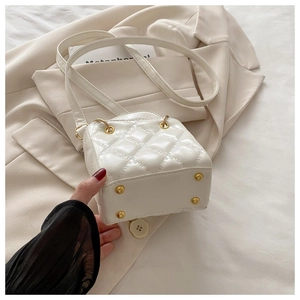 Detail van witte gewatteerde crossbodytas met gouden noppen op een beige blazer achtergrond