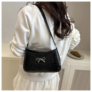 Detailed view of black crocodile pattern underarm bag with a silver bow buckle on model