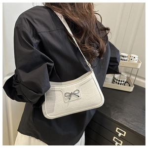 Close-up of white crocodile texture faux leather baguette bag with silver bow ornament