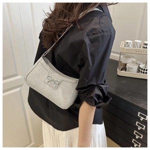 Detail of silver glitter shoulder bag with metallic bow accessory on black fabric background