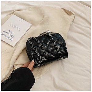 Close-up of black quilted chain bag on tweed jacket with silver hardware and leather texture