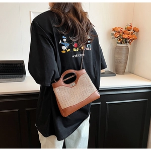 Detail of a brown leather and straw bucket bag with gold chain and metal twist lock