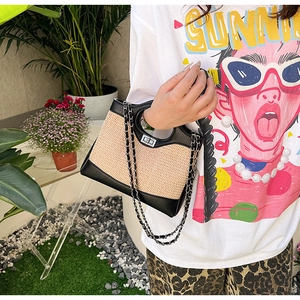 Detail of straw bucket bag with black leather trim and chain strap on outdoor model