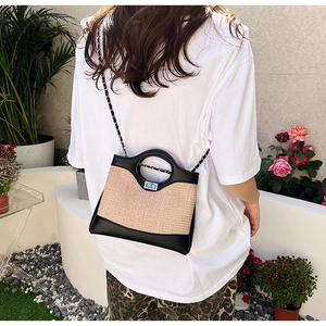 Fashionable beige woven bucket bag with black leather trim and chain strap on a model
