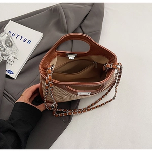 Detail view of straw and leather bucket bag featuring chain strap and zipped inner pocket