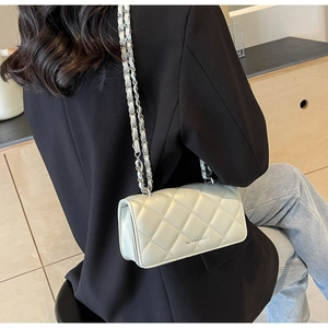 Close-up of beige quilted crossbody bag with silver chain strap and metal lettering
