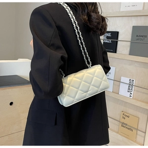 Detail of white quilted crossbody bag with silver chain strap and metal branding text