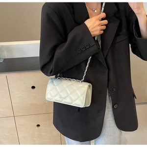 Close-up of quilted chain crossbody bag styled with a black blazer and grey jeans
