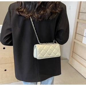 Detail of a beige quilted crossbody bag with a silver chain strap worn by a model