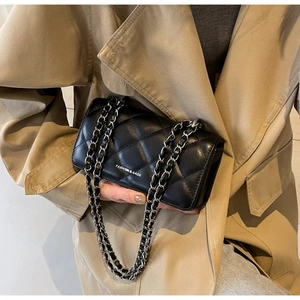 Detail of black quilted crossbody bag with silver chain strap and fashion text