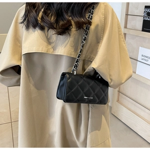 Close-up of black quilted crossbody bag with silver chain strap worn over a trench coat