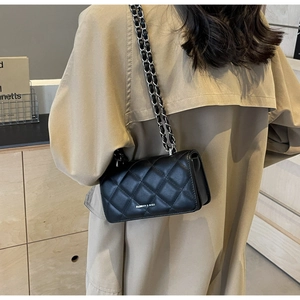 Close-up of black quilted leather shoulder bag with silver chain strap on beige trench coat
