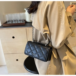 Detail of black quilted chain bag with silver hardware on khaki trench coat