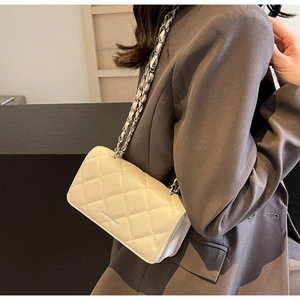 Detail of quilted diamond pattern crossbody bag with silver chain strap on model