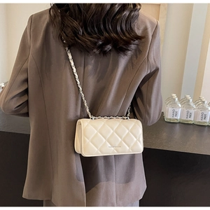 Detail of cream quilted crossbody bag with silver chain strap shown on person